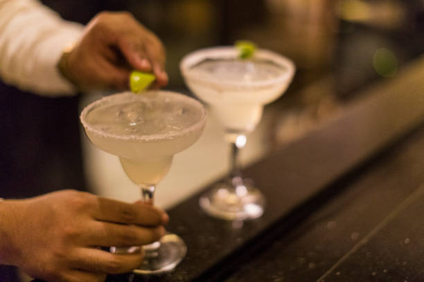 Close-up of an unrecognizable Panamanian bartender putting the final touch on a margarita cocktail by placing a lime wedge on the glass rim. stock photo