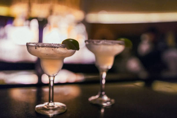 Close-up of two cold and delicious Margarita cocktails on a bar counter with a lime wedge on the glass rim.
