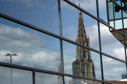 The tower of Ulm Minster is reflected in the glass façade of a building