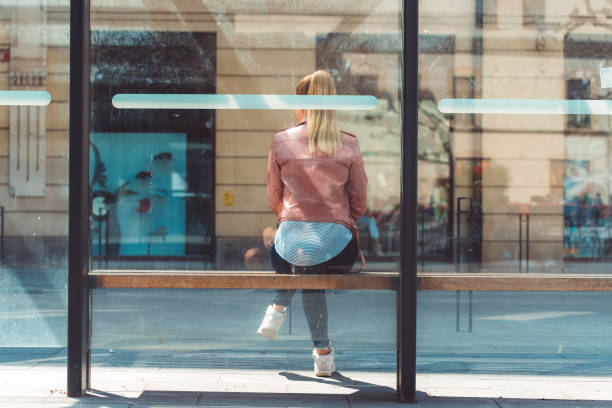 Young woman sitting and waiting at the bus station in the city centr on a sunny spring day