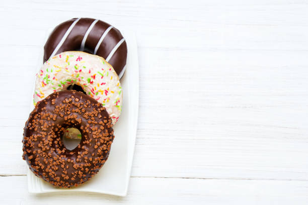 istock Tasty bitten donuts with icing and chocolate on white wooden background, copy space 672222710
