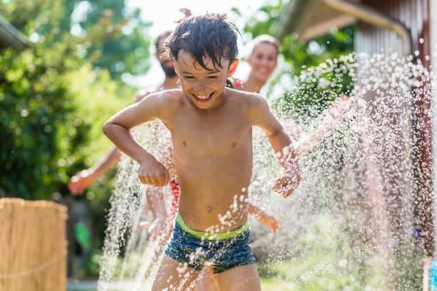 niño de enfriamiento con las manguera de jardín, familia en el fondo - enfriamiento fotografías e imágenes de stock