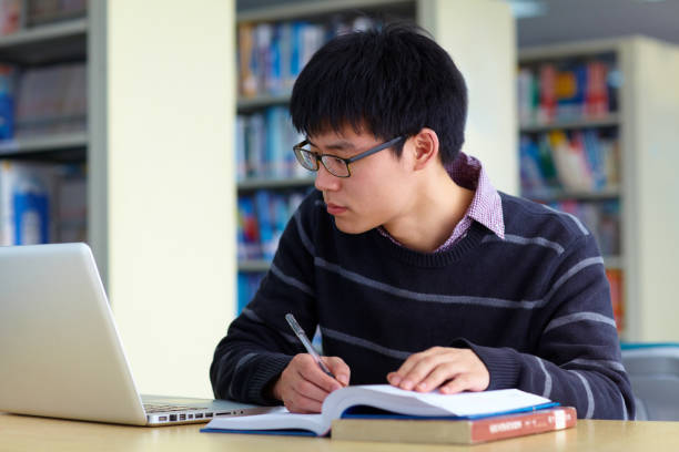 istock One male asian college student study in the library with laptop on table 672236566