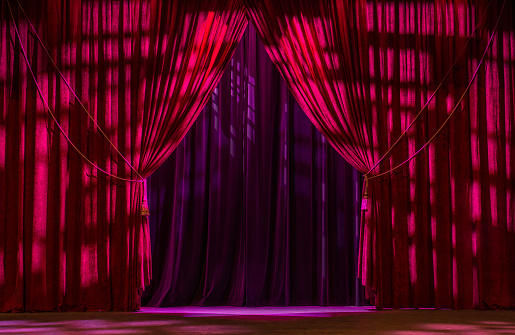 Red open theatre curtain with gold tassels agains a purple curtain.