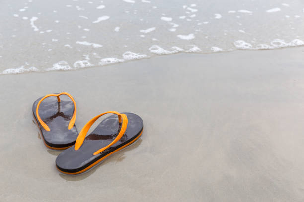 chaussons de plage bruns et orange sur plage de sable de l’océan, concept de vacances d’été. - sandy brown photos photos et images de collection