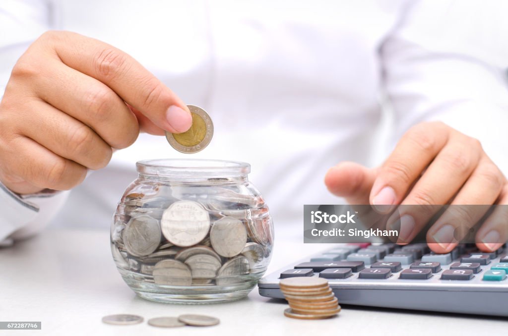 Male hand putting money coins into glass jar bank Male hand putting money coins into glass jar bank for saving money concept Accountancy Stock Photo