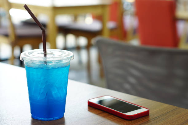 closeup cocktail ou desses tropical - copo plástico de blue hawaii italiano soda com limão e moblie telefone na mesa de madeira. - blue blueberry cold food descriptive color - fotografias e filmes do acervo