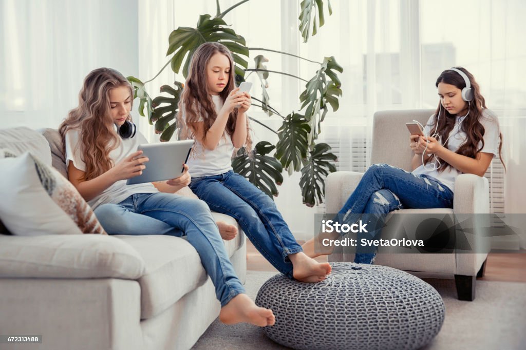Kids with phones and tablets, with smartphones and headphones. Group of teenage girls is using gadgets. Education, friendship, technology and children concept. Group of teenage girls is using gadgets. Kids with phones and tablets, with smartphones and headphones. Family Stock Photo