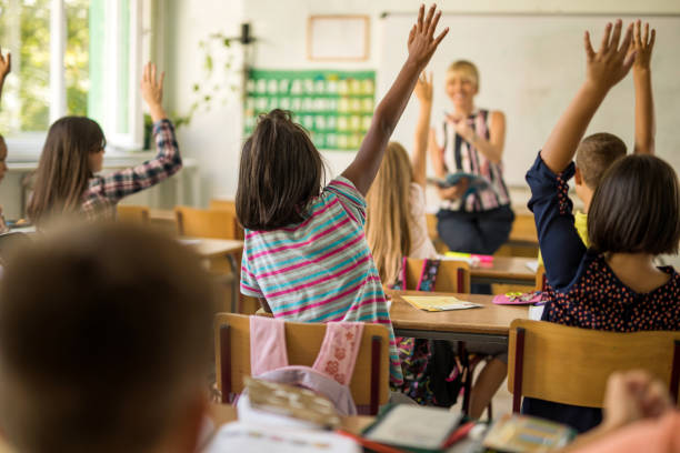 istock Rear view of elementary students with raised hands in classroom. 672313762
