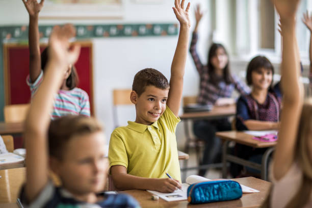 istock Little boy and his classmates with raised arms in classroom. 672315244