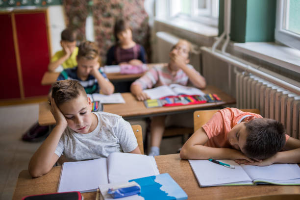Group of bored elementary students in the classroom. Group of tired school kids feeling bored while sitting in the classroom during the lecture. boredom stock pictures, royalty-free photos & images