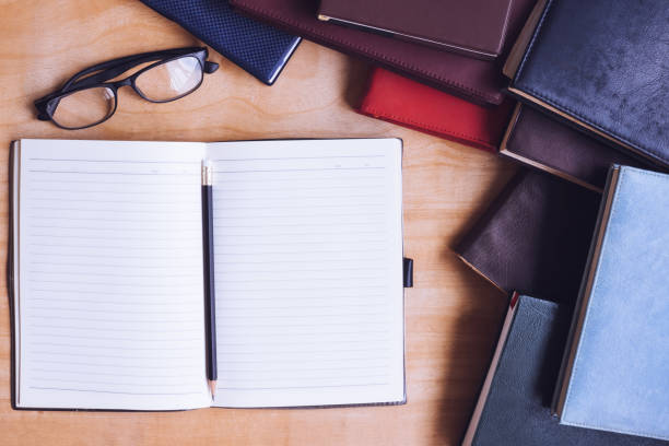 istock Blank notebook with pencil, glasses and books on wooden table. 672324584