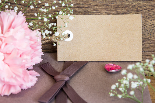 Blank paper tag with carnation flower on wooden background
