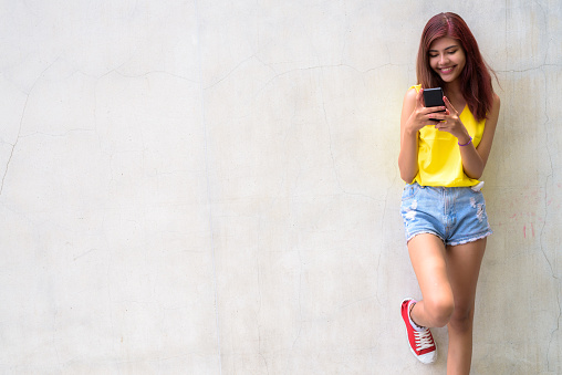 Portrait of happy young beautiful teenage girl smiling against concrete wall horizontal shot