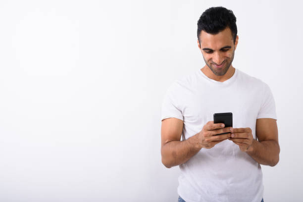 istock Studio shot of happy young handsome Indian man smiling while using mobile phone against white background 672331460