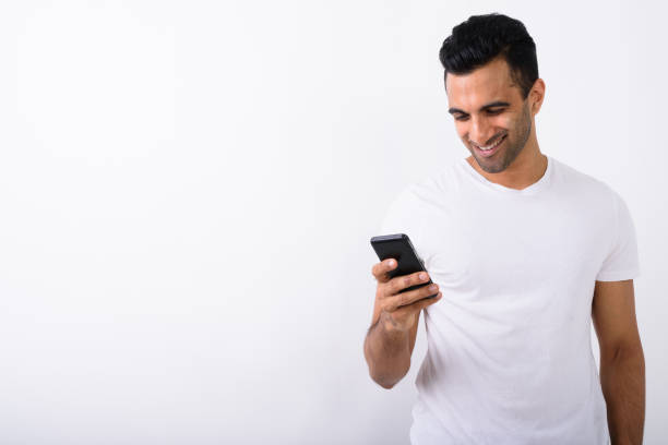 istock Studio shot of happy young handsome Indian man smiling while using mobile phone against white background 672331464