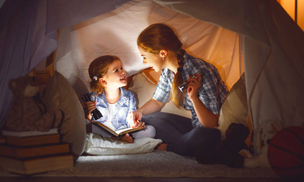 istock mother and child daughter with a book and a flashlight before going to bed 672343262