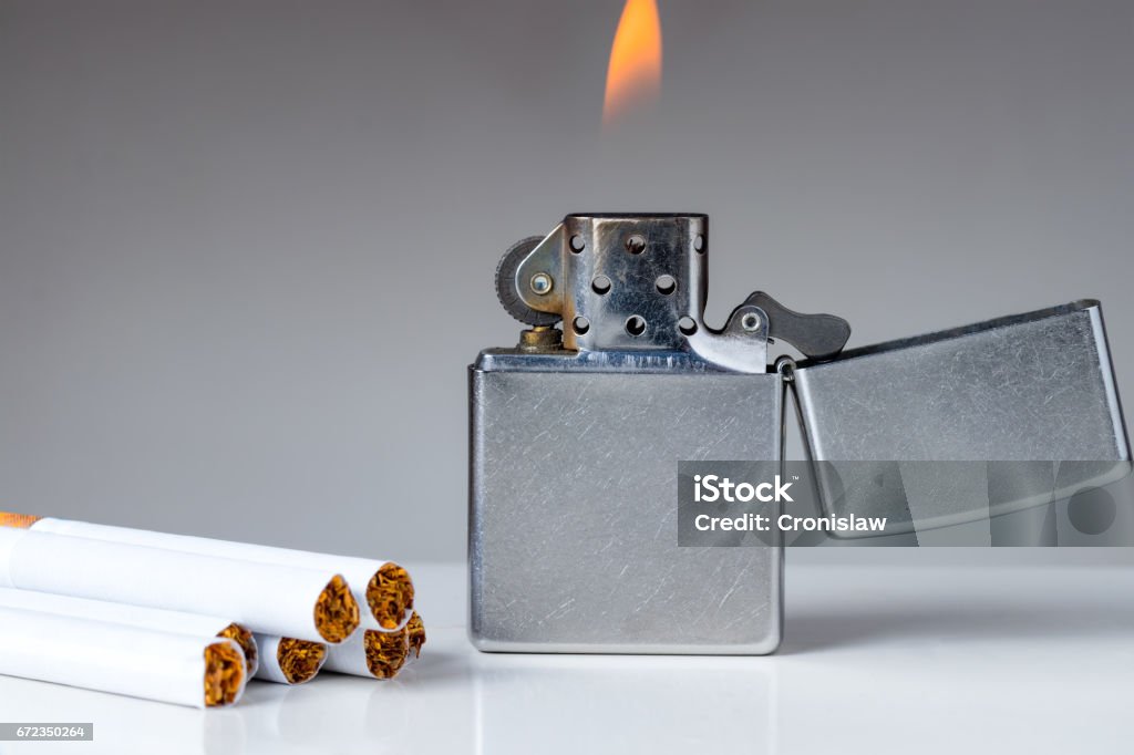 Cigarettes and lighter with flame on white and grey background. Cigarettes and lighter with flame on white and grey background. Nicotine and tobacco addiction abstract concept. Copy space on the left. Burning Stock Photo