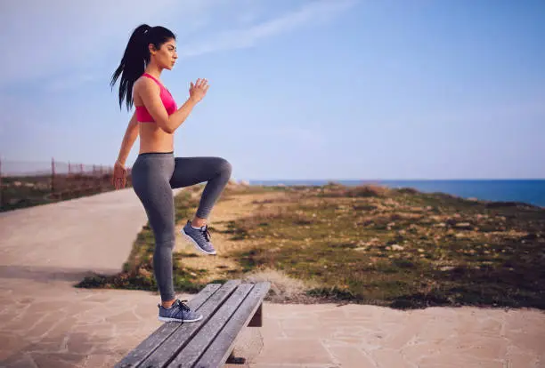 Photo of Young fit brunette woman doing steps on a bench outdoors