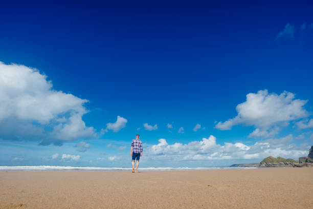 istock Man walking along Watergate Bay beach on a beautiful day. 672388532