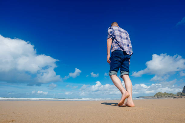 man in rolled up jeans, and plains shirt walking along Watergate Bay Beach, Newquay, Cornwall on a beautiful sunny late September day.