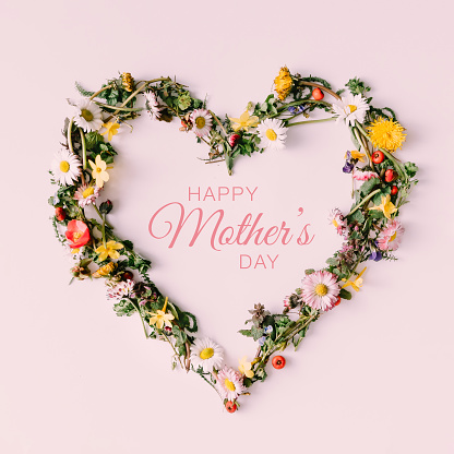 Heart symbol made of flowers and leaves with happy Mothers day text on white background.
