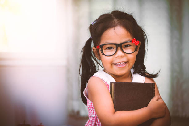 menina asiática feliz abraçando um livro - child glasses elementary student reading - fotografias e filmes do acervo