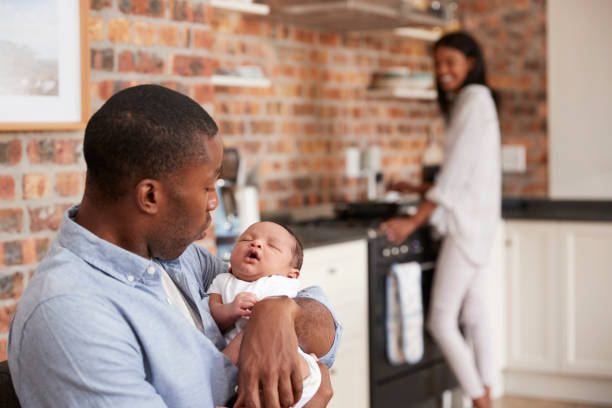 istock Father Holding Newborn Son As Mother Makes Meal 672419688