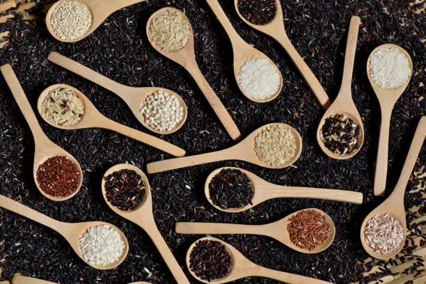 Top view different rice on wooden scoop with black riceberry background, Various rice organic on wooden spoon collection