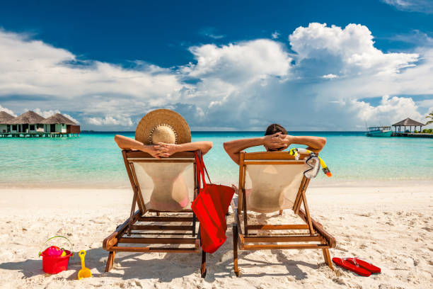 couple in loungers on beach at maldives - turizm fotoğraflar stok fotoğraflar ve resimler
