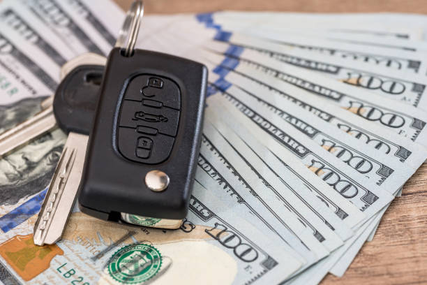 istock Car key lying on US 100 dollar bills on wooden desk. 672429180