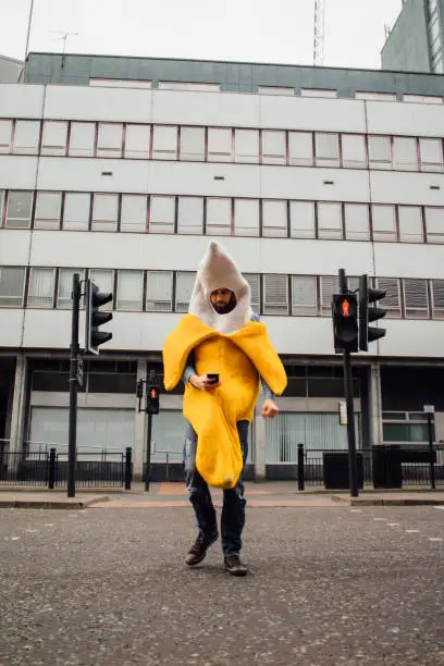 Man wearing a banana costume is distracted by his phone whilst crossing the road, not realising that the crossing is on a red man indicating he wasn't looking.