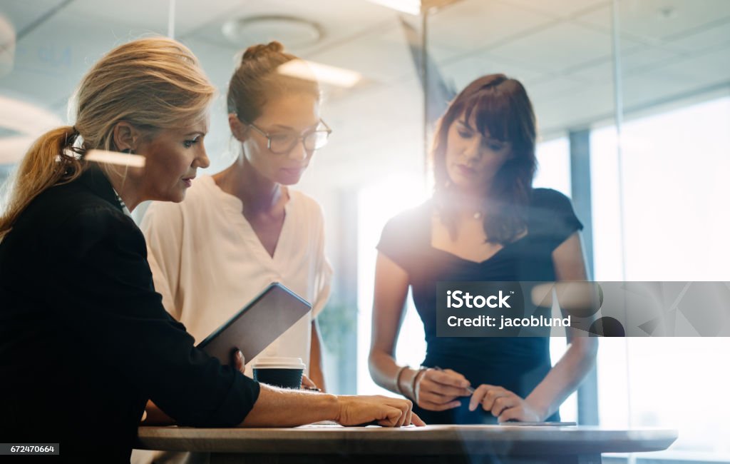 Businesswomen brainstorming over new business ideas Three businesswomen standing at the table and discussing new projects. Corporate professionals brainstorming over new business ideas. Women Stock Photo