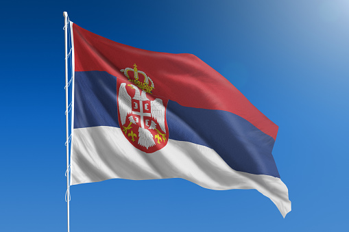 The National flag of Serbia blowing in the wind in front of a clear blue sky