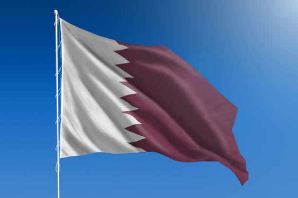National flag of Qatar on clear blue sky The National flag of Qatar blowing in the wind in front of a clear blue sky qatar flag stock pictures, royalty-free photos & images