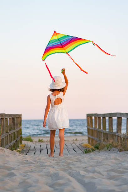 Girl play with rainbow colorful kite on the beach at sunset stock photo