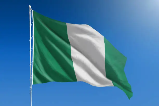 The National flag of Nigeria blowing in the wind in front of a clear blue sky