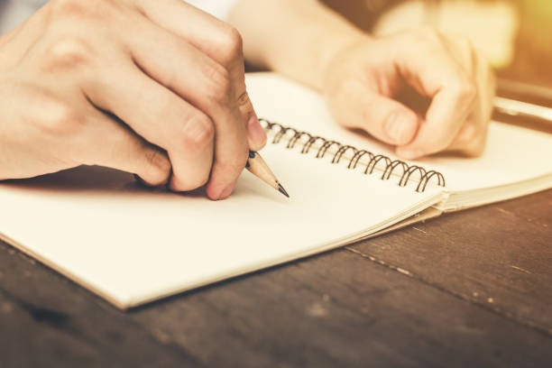 istock hand woman writing notebook with pencil on wood table. 672483640