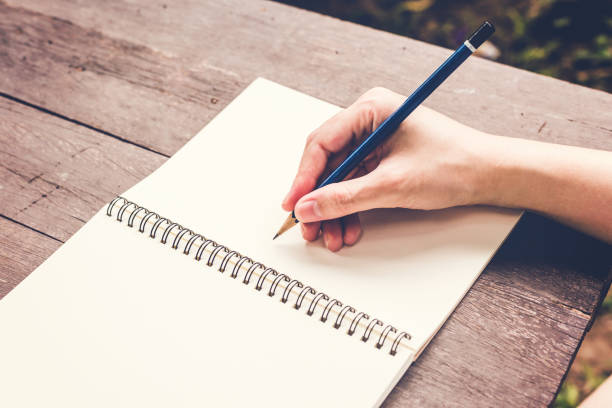 istock hand woman writing notebook with pencil on wood table. 672485828
