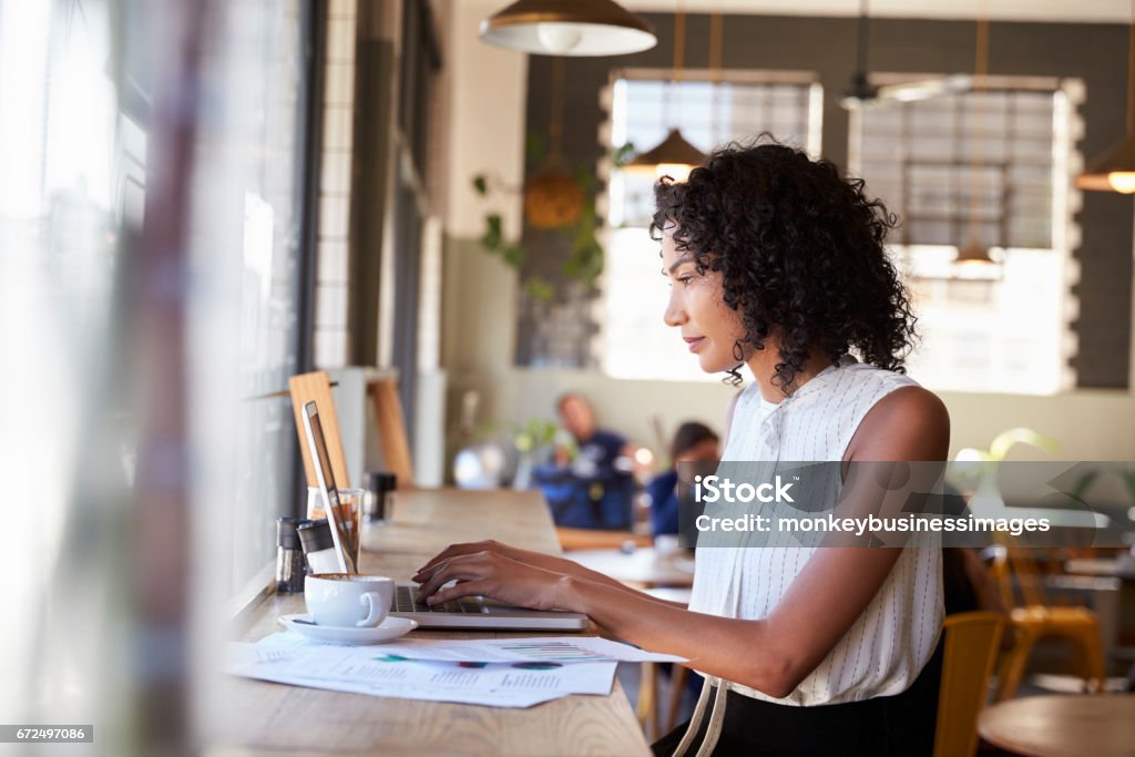 Businesswoman By Window Working On Laptop In Coffee Shop Working Stock Photo