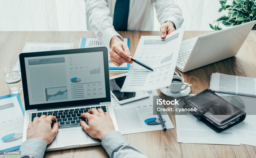 Business partners in the office Business partners working at office desk, one is showing financial data on a report to his colleague, point of view shot Financial Report Stock Photo