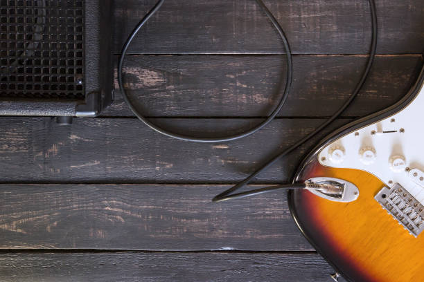 istock Electric guitar and black amplifier connected by cable on wooden floor 672531498