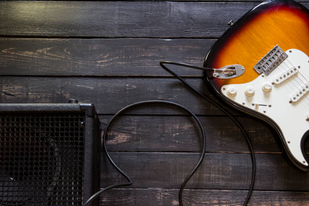 istock Electric guitar with amplifier connected by cable on wooden background 672531546