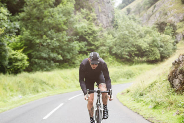 istock Tattooed road cyclist dressed in black, attacking a climb 672546070