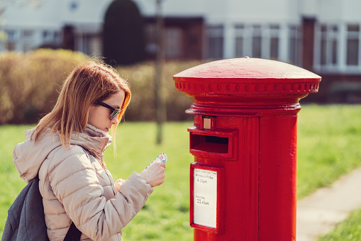 Young woman in the city posting letters in the mailbox