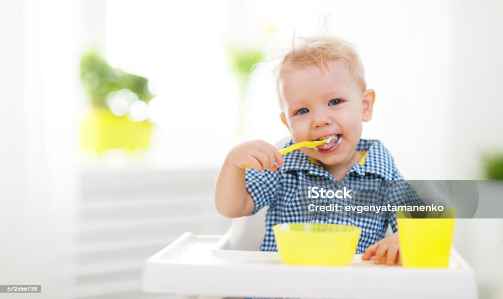 Happy baby eating himself Happy baby eating himself with a spoon Eating Stock Photo