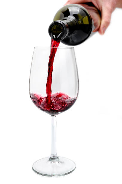 istock Red wine poured from a bottle in a elegant crystal goblet, isolated on white background. 672582546