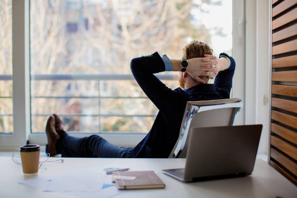 homme d’affaires assis au bureau et en regardant par la fenêtre - hands behind head photos et images de collection