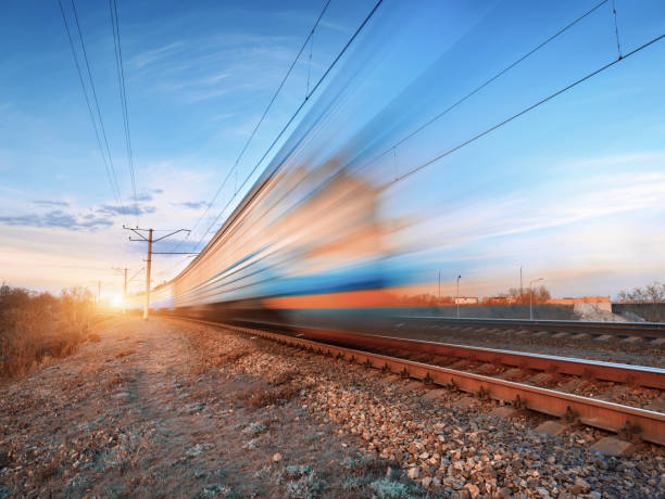istock High speed train in motion on railroad track at sunset. Blurred commuter train. Railway station against colorful blue sky. Railroad travel, railway tourism. Rural industrial landscape in twilight 672603868