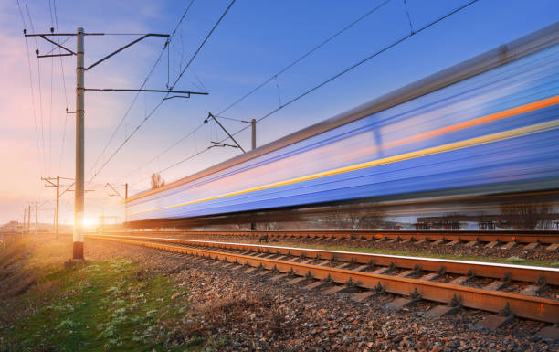 istock High speed passenger train in motion on railroad at sunset. Blurred commuter train. Railway station against colorful blue sky. Railroad travel, railway tourism. Rural industrial landscape. Concept 672603874